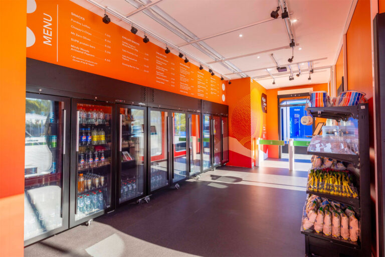 A pop-up store with fridges and overhead lighting and turnstiles at the exit.