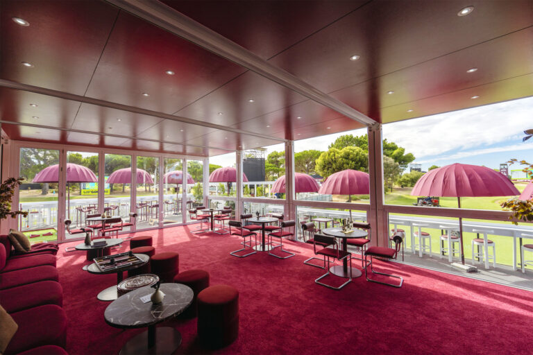 a room with floor to ceiling windows overlooking a golf course and deck area with tables and chairs and umbrellas